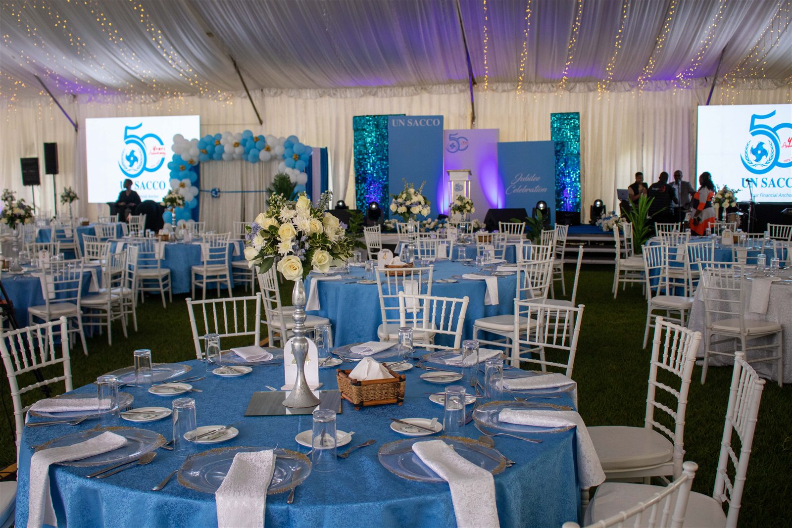 Decorated tables and UN SACCO 50th anniversary stage inside a marquee